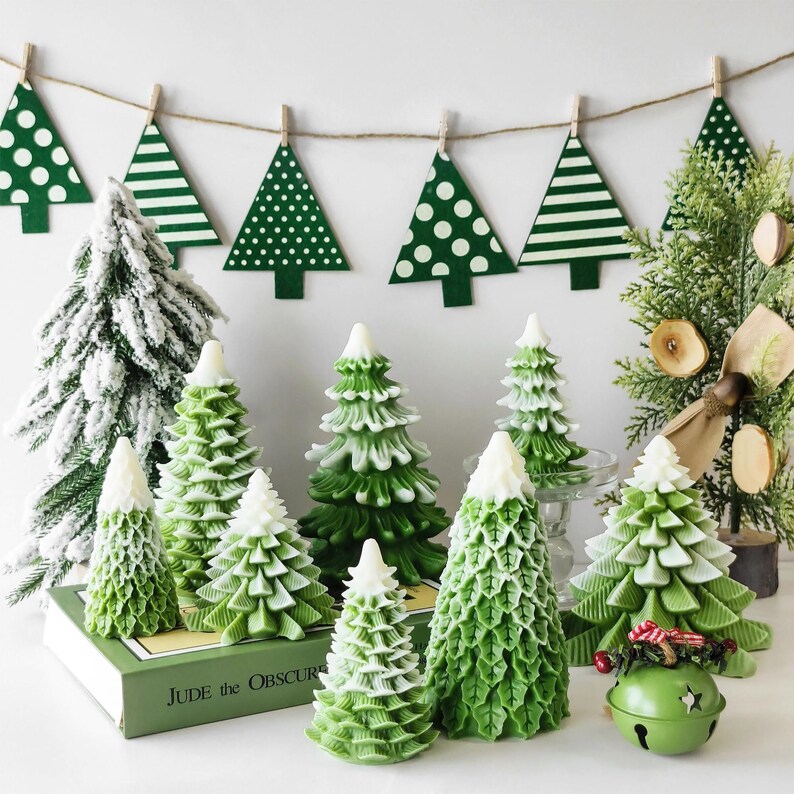 May include: A collection of green and white Christmas tree candles, some with a frosted finish, arranged on a table with a book titled "Jude the Obscure".