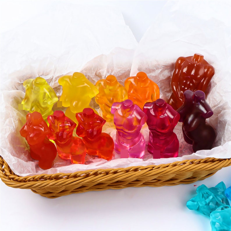 Op de afbeelding: Een mand gevuld met kleurrijke gummy snoepjes in de vorm van menselijke torso's. De snoepjes zijn gerangschikt in een regenboogpatroon, met rode, oranje, gele, groene, blauwe en paarse snoepjes.