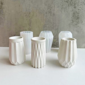 May include: Six white geometric concrete planters with a textured, diamond-shaped pattern. The planters are arranged in a row on a white surface.