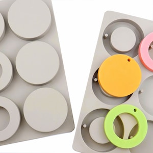 May include: Two silicone molds for making resin jewelry. The mold on the left has six round cavities, while the mold on the right has six round cavities with a raised ring around each. The mold on the right also has a small hole at the top of each cavity for adding a jump ring.