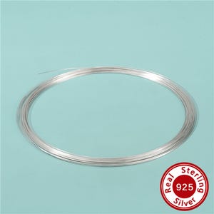 May include: A continuous coil of thin, metallic silver wire arranged in a circular loop. A circular red and white emblem in the bottom right corner features the text Real Sterling Silver and the number 925 in the centre of the design.