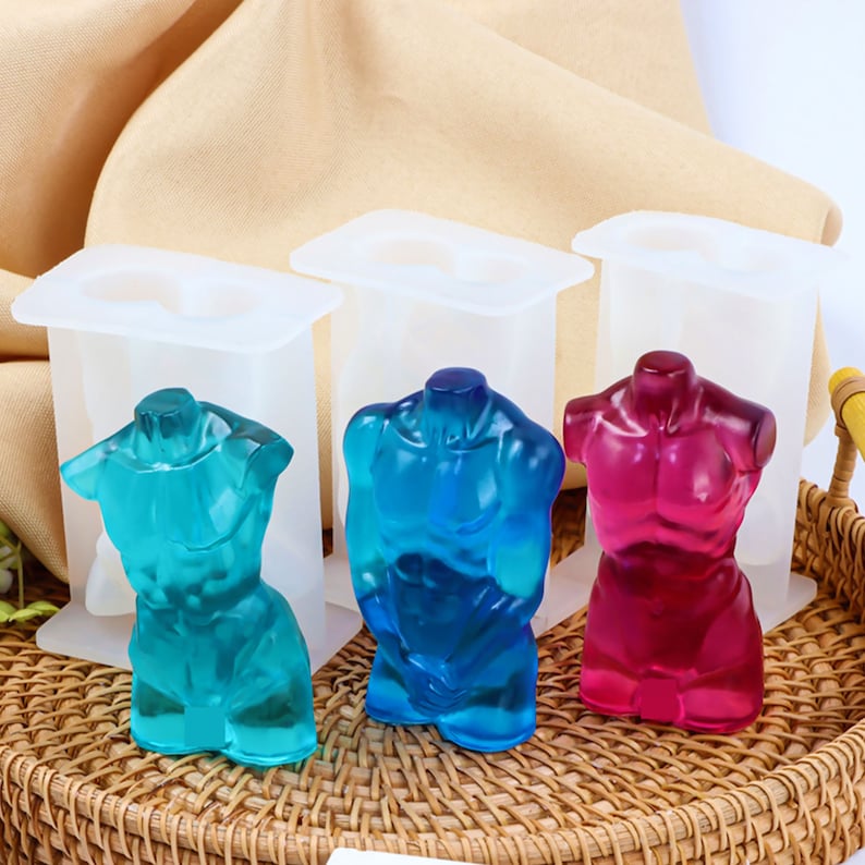 Op de afbeelding: Drie siliconen mallen voor het maken van harsfiguren. De mallen zijn wit en hebben een rechthoekige vorm. De figuren bevinden zich in de mallen en zijn gemaakt van helder hars. De figuren zijn blauw, rood en lichtblauw. De figuren zijn in de vorm van een menselijk torso.