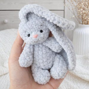 Op de afbeelding: Een lichtgrijs, pluche konijn met lange oren, zwarte ogen en een roze neus. Het handgemaakte knuffeldier is zacht en knuffelig, perfect als kinderspeelgoed of voor de inrichting van de kinderkamer. Het konijn is gemaakt van een getextureerd, pluizig materiaal.