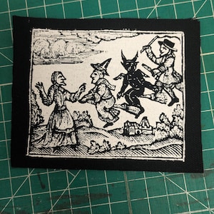 May include: A black and white patch featuring a vintage illustration of witches flying on brooms with a devil figure. The artwork is framed by a black border, creating a striking contrast. The patch is likely for clothing or accessories.