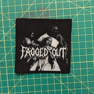 May include: Black fabric patch with the words "FAGGED OUT" in white, gothic-style lettering. The patch features a grayscale image of figures. The patch is square and appears to be made of woven material.