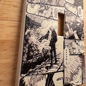 Può includere: Una custodia bianca per telefono con un design in stile manga in bianco e nero. I pannelli raffigurano scene e personaggi, con fumetti e la parola "NEXT". La custodia ha una superficie strutturata.