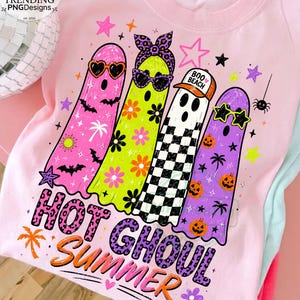 May include: A light pink t-shirt featuring a graphic of four ghosts. The ghosts are pink, lime green, white with a black checkerboard pattern, and purple. They wear sunglasses, a headband, and a hat that says BOO BEACH. The text reads HOT GHOUL SUMMER.