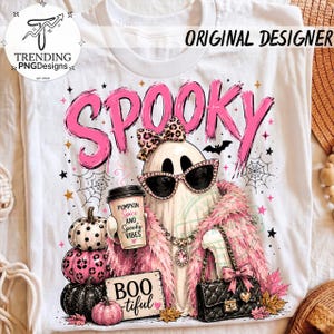 May include: A white t-shirt featuring a graphic of a ghost wearing leopard print sunglasses and a matching bow, holding a coffee cup labeled Pumpkin Spice and Spooky Vibes. The ghost wears a pink feather boa and carries a black quilted handbag.