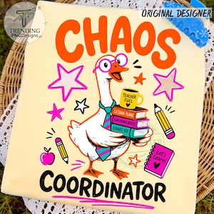 May include: A light yellow t-shirt featuring a graphic of a white goose wearing pink glasses and a teal and pink striped tie. The goose holds a stack of books labeled Lesson Plans, Surviving Recess, and Chaos 101, topped with a yellow Teacher Fuel mug.