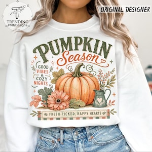 May include: A white crewneck sweatshirt featuring a graphic print with the text PUMPKIN SEASON, GOOD VIBES & COZY NIGHTS, and FRESH PICKED, HAPPY HEARTS. The design includes a large orange pumpkin, a flower, and a small pitcher with a heart.
