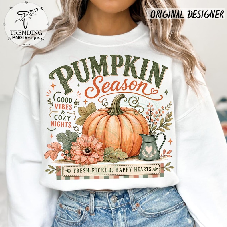 May include: A white crewneck sweatshirt featuring a graphic print with the text PUMPKIN SEASON, GOOD VIBES & COZY NIGHTS, and FRESH PICKED, HAPPY HEARTS. The design includes a large orange pumpkin, a flower, and a small pitcher with a heart.