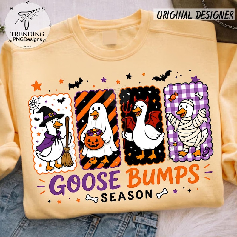 Op de afbeelding: Een lichtgeel sweatshirt met ronde hals en een afbeelding van vier eenden in Halloween-kostuums: een heks, een geest met een pompoen, een duivel en een mummie. De tekst GOOSE BUMPS SEASON staat onder de eenden, omringd door sterren en vleermuizen.