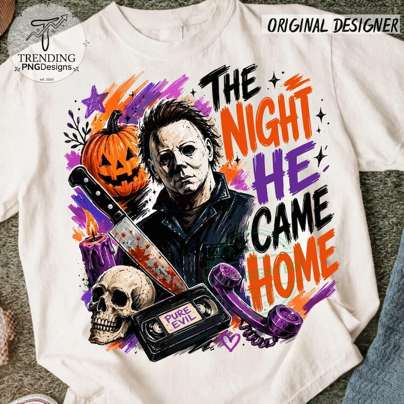 Puede incluir: Una camiseta blanca con un gr&aacute;fico de un personaje de pel&iacute;cula de terror, una calabaza, una calavera, un cuchillo, una cinta VHS con la etiqueta PURE EVIL y un tel&eacute;fono morado. El texto THE NIGHT HE CAME HOME aparece en letras naranja y moradas.