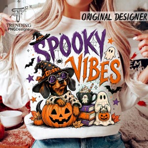 Könnte beinhalten: Ein weißes Sweatshirt mit einer Grafik eines Dackels, der einen Hexenhut und eine runde Brille trägt und in einem Kürbis sitzt. Der Text lautet SPOOKY VIBES, ergänzt durch Illustrationen von einem Geist, einer Tasse, Büchern, Fledermäusen und Sternen.