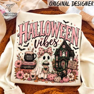 May include: A cream-colored sweatshirt featuring a graphic print with the text "HALLOWEEN vibes". The design includes a ghost with a pink bow holding a coffee cup, a black cat, a haunted house, a cauldron, books, pumpkins, and flowers.