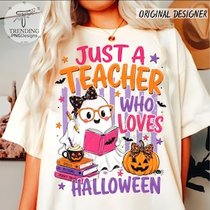 May include: A cream-colored t-shirt featuring a graphic of a ghost wearing glasses and a bow, reading a pink book, holding a pencil, and sitting next to a stack of books and a jack-o'-lantern. The text reads JUST A TEACHER WHO LOVES HALLOWEEN.