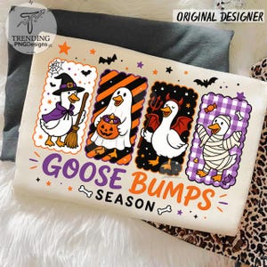 Op de afbeelding: Een cr&egrave;mekleurig T-shirt met vier rechthoekige panelen met cartoon-ganzen verkleed voor Halloween: een heks, een geest met een pompoen, een duivel en een mummie. De tekst "GOOSE BUMPS SEASON" staat in paarse en oranje letters onder de panelen.