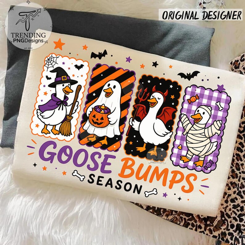 Op de afbeelding: Een cr&egrave;mekleurig T-shirt met vier rechthoekige panelen met cartoon-ganzen verkleed voor Halloween: een heks, een geest met een pompoen, een duivel en een mummie. De tekst "GOOSE BUMPS SEASON" staat in paarse en oranje letters onder de panelen.