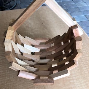 May include: A handcrafted wooden basket with a unique geometric design. The basket is constructed from various shades of natural wood, creating a visually appealing contrast. The open weave allows for air circulation, and the handle adds a functional element.