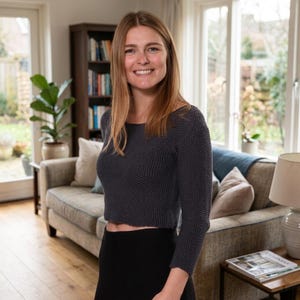 May include: A dark charcoal gray long-sleeved sweater with a textured knit pattern. The sweater features a wide, rounded neckline and a cropped hemline that sits above the waist. The garment is constructed with a consistent, dense knit stitch.
