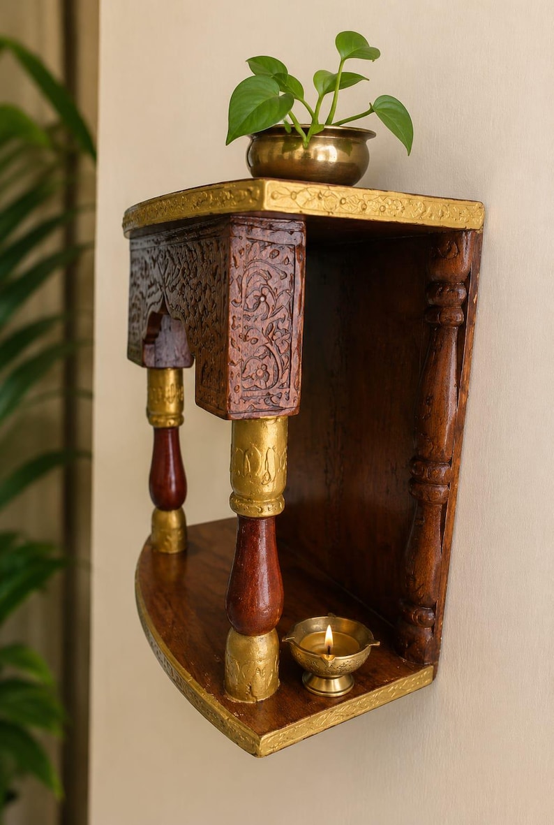 K&ouml;nnte beinhalten: Ein wandmontiertes Holzregal aus dunkelbraunem Holz mit goldfarbenen Akzenten, aufwendigen Blumenverzierungen am oberen Rahmen und zwei gedrechselten S&auml;ulen. Oben steht eine kleine Messingschale mit einer gr&uuml;nen Pflanze, unten eine brennende &Ouml;llampe.