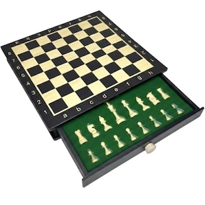 Op de afbeelding: Een zwart en bruin houten schaakset met een lade met schaakstukken. Het schaakbord is open en onthult een met groen vilt gevoerde lade met ivoorkleurige schaakstukken. Het bord heeft zwarte en bruine vierkanten en is genummerd en geletterd.
