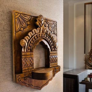 May include: A detailed wooden wall shelf, featuring an arched design and ornate carvings. The shelf is a rich brown hue, with floral and geometric patterns. It's mounted on a neutral wall, highlighting its decorative nature and craftsmanship.