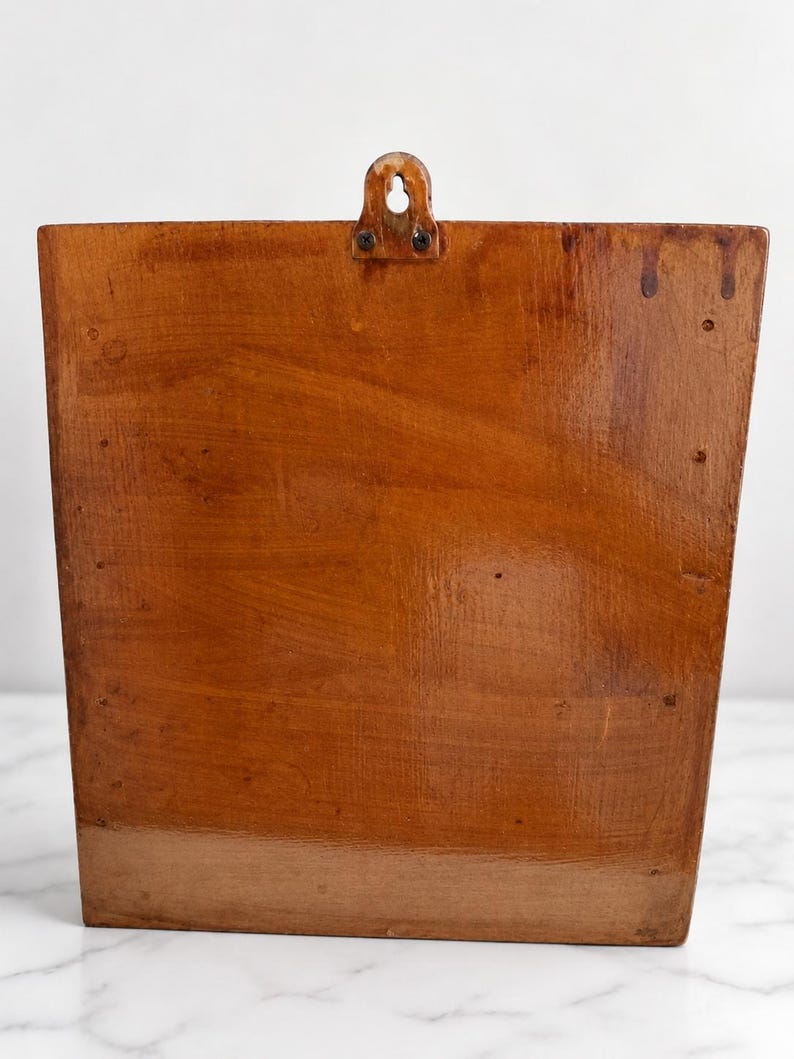 K&ouml;nnte beinhalten: Ein rechteckiger Wandhalter aus Holz mit polierter, mittelbrauner Oberfl&auml;che. Das St&uuml;ck weist eine sichtbare Holzmaserung, eine flache Vorderseite und eine Metallaufh&auml;ngung auf, die mit zwei kleinen Schrauben oben mittig befestigt ist.
