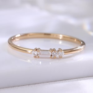 Peut inclure: Une fine bague en or ornée d'un diamant central taille baguette disposé horizontalement, encadré de deux petits diamants taille ronde de chaque côté. L'anneau est lisse et poli, présentant un design délicat avec des pierres étincelantes.