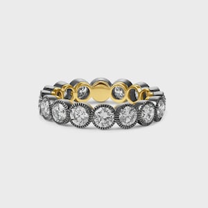 May include: A ring featuring a continuous band of round, clear, faceted stones set in a dark, textured metal frame. The interior of the band is finished in a smooth, polished gold tone, creating a contrast between the dark exterior and gold inner surface.