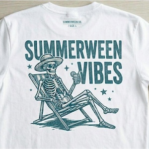 Może przedstawiać: Biały t-shirt z turkusową grafiką szkieletu w kapeluszu przeciwsłonecznym i okularach, wypoczywającego na leżaku z napojem. Napis głosi SUMMERWEEN CO. / SIZE L u góry oraz SUMMERWEEN VIBES na środku, w otoczeniu gwiazdek.