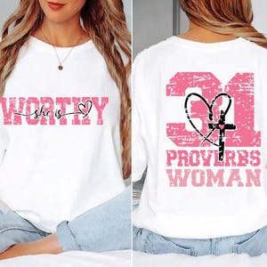 May include: White sweatshirt with the words "WORTHY she is" in pink, with a heart symbol. The back of the shirt features the number "31", a heart, a cross, and the words "PROVERBS WOMAN" in pink.