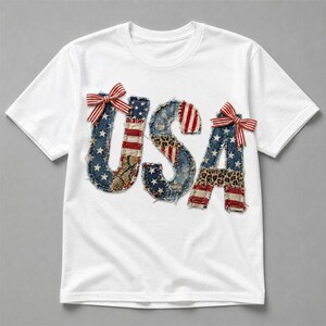 Könnte beinhalten: Ein weißes Kurzarm-T-Shirt mit den Buchstaben USA als Applikation auf der Vorderseite. Die Buchstaben bestehen aus verschiedenen Stoffstücken mit Sternen-, Streifen- und Tiermustern, ausgefransten Kanten und rot-weiß gestreiften Schleifen.