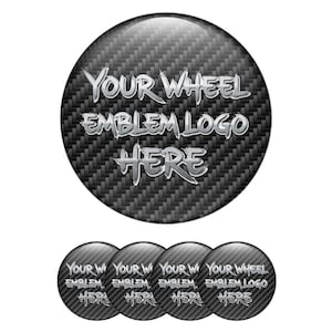 May include: A set of four circular car emblems with a carbon fiber texture. The main emblem has the text "YOUR WHEEL EMBLEM LOGO HERE" in a silver, metallic font. The smaller emblems repeat the same text.