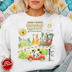 May include: White sweatshirt featuring a colorful graphic of Mickey and Minnie Mouse in a red car, with a train and the text "Mickey & Minnie's Runaway Railway 5th Anniversary". The design includes a sun, mountains, and a road.