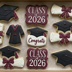 Puede incluir: Surtido de galletas con temática de graduación en una caja. Las galletas incluyen birretes, diplomas con lazos, togas de graduación y galletas con el texto "Class of 2026" y "Congrats". Las galletas están decoradas con glaseado negro, blanco y burdeos.