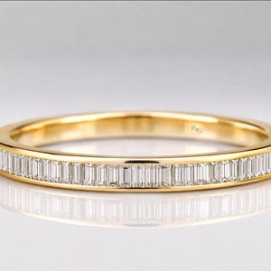 May include: A yellow gold band ring featuring a continuous channel setting of clear, rectangular baguette-cut diamonds encircling the entire outer circumference. The interior of the band displays a small, engraved logo reading P&G.