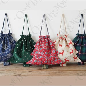 Op de afbeelding: Vijf kerstboomvormige tassen met trekkoord in verschillende feestelijke patronen. Ontwerpen omvatten sneeuwvlokken, sterren, paisley, rendieren en ruitjes. Elke tas heeft een bijpassend trekkoord.
