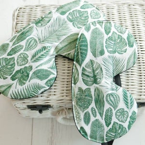 May include: Two green and white sleep masks with a tropical leaf pattern. The masks are made of soft fabric and have an elastic strap.
