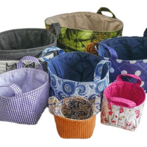 May include: A set of six fabric storage baskets in various colors and patterns. The baskets are made of quilted fabric and have a variety of designs, including polka dots, paisley, and floral prints.