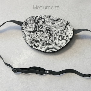 May include: Black and white paisley eye patch with a black elastic strap. The strap has an adjustable buckle. Medium size.