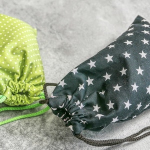 Peut inclure: Deux sacs à cordon, l'un vert à pois blancs et l'autre noir à étoiles blanches.