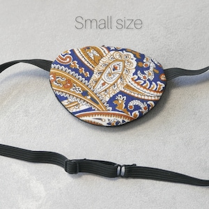 May include: A blue and gold paisley eye patch with an adjustable black elastic strap. The strap has a metal slider to adjust the fit. The text "Small size" is visible above the eye patch.