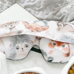 May include: A sleep mask featuring a repeating pattern of woodland animals including a hedgehog, a fox, and an owl. The fabric has a white background with soft-toned illustrations of the animals' faces. A black elastic strap is attached to the sides.