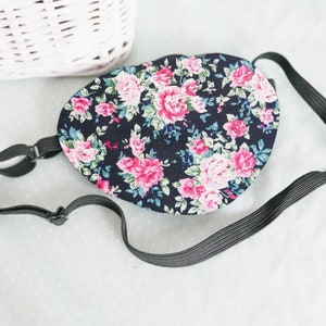 May include: A black eye mask with a floral pattern featuring pink roses and green leaves. The mask has an adjustable elastic strap.