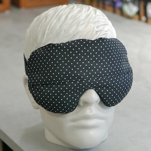 May include: A black sleep mask with white polka dots. The mask is made of soft fabric and is designed to block out light.