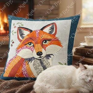 Puede incluir: Coj&iacute;n decorativo cuadrado con un dise&ntilde;o de zorro colorido. El zorro tiene detalles de patchwork en naranja, rojo y rosa. El coj&iacute;n tiene un borde azul con lunares blancos. Un gato blanco descansa frente al coj&iacute;n.
