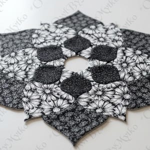 May include: A black and white floral placemat in a starburst design. The placemat features a variety of patterns, including daisy prints and small floral motifs. The centre has a circular opening. The placemat is made of fabric.