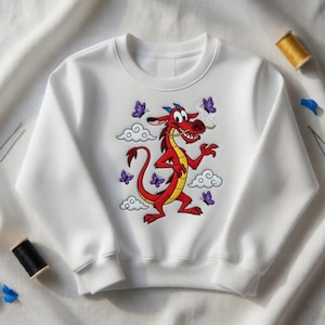 May include: White crewneck sweatshirt featuring a cartoon dragon design. The dragon is red and yellow, with a long tail and a mischievous expression. Purple butterflies and white clouds surround the dragon. The sweatshirt is made of a soft material.