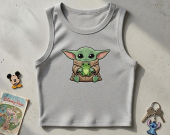 May include: A light gray ribbed tank top featuring a cartoon image of a green alien-like character holding a green frog. A Mickey Mouse pin, a Disney Park map, and a Stitch keychain are also visible.